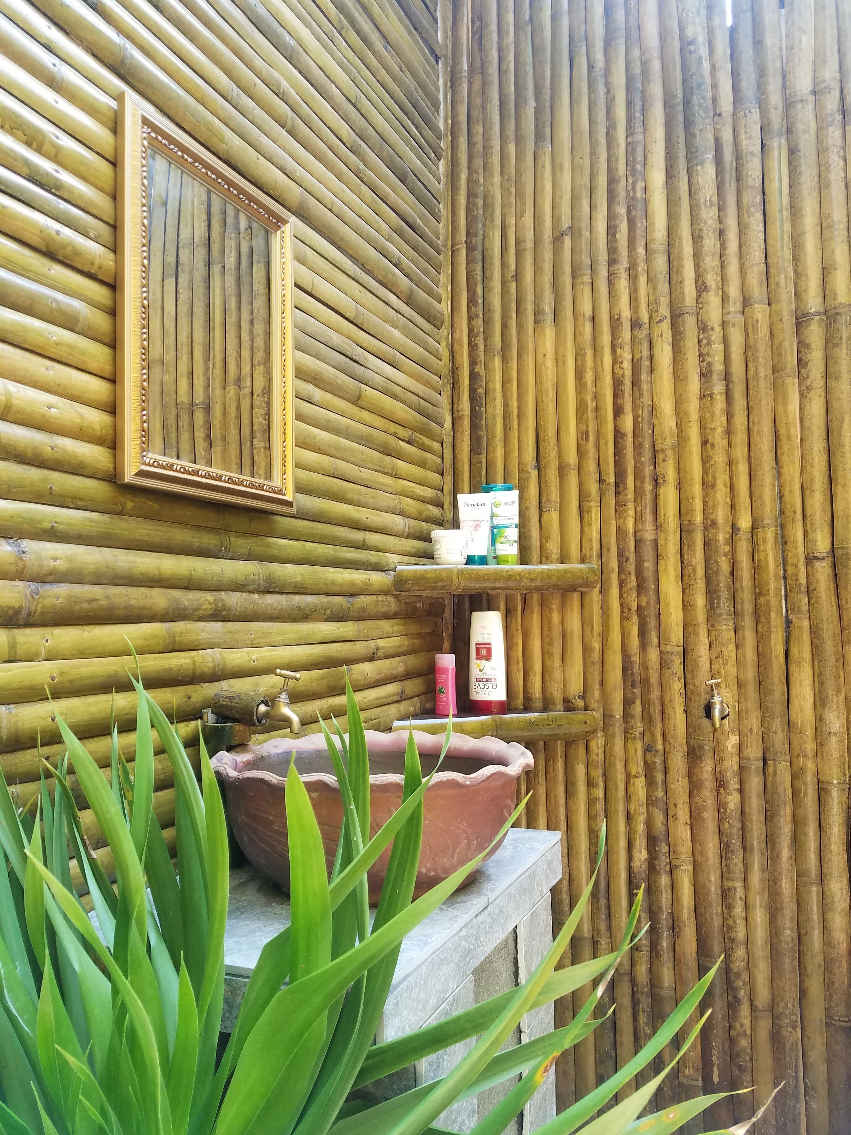 Un baño con pared de bambú, un espejo, un lavabo y artículos de aseo.