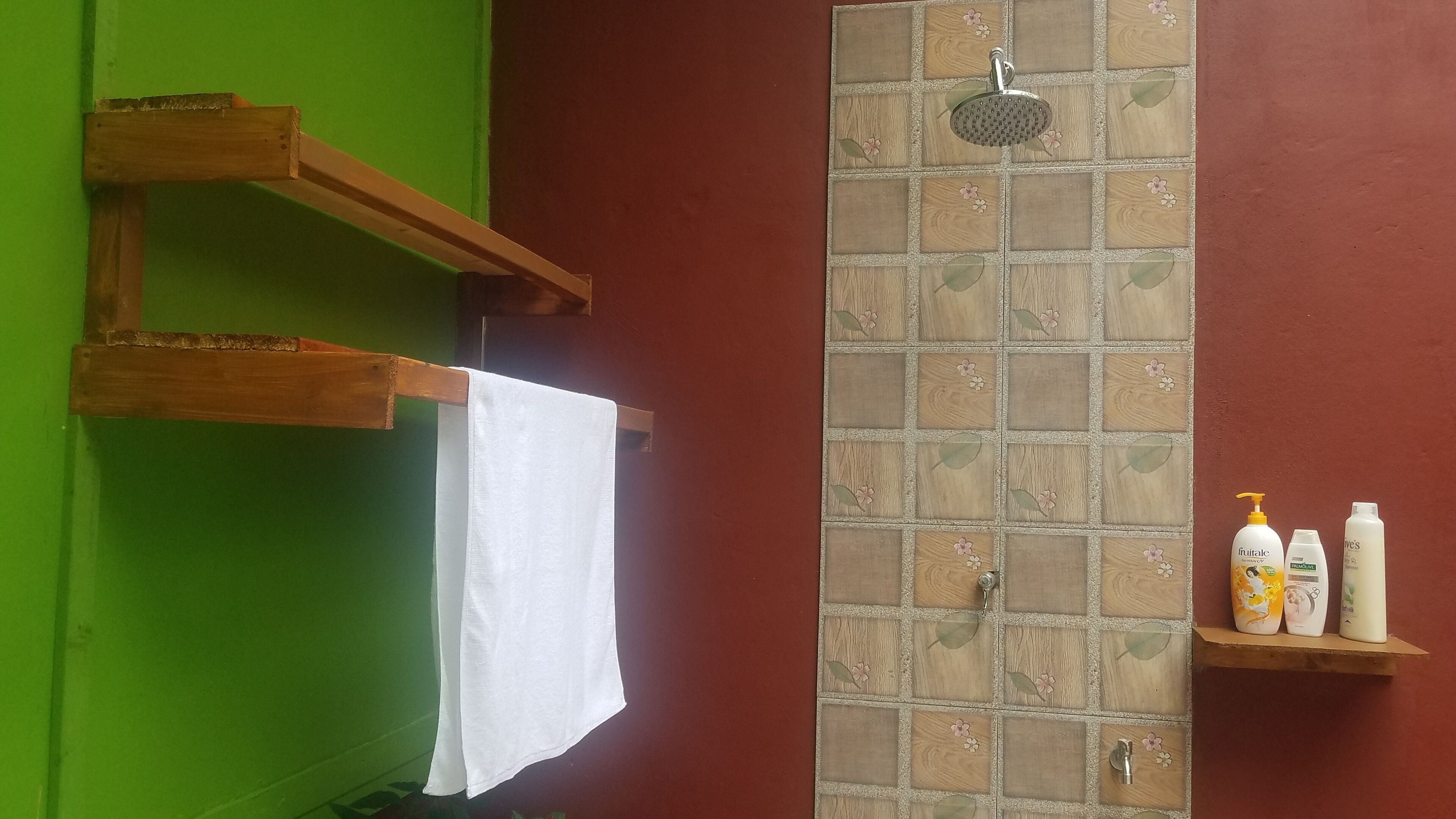 A bathroom with a shower, a towel hanging on a rack, and toiletries on a shelf.