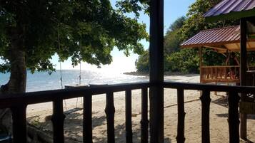 A beach view from a wooden deck with a metal railing, overlooking a sandy beach and the ocean.