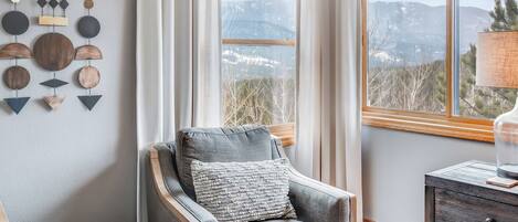 A cozy room with a grey armchair, a round wooden table, and a wall-mounted wooden art piece.