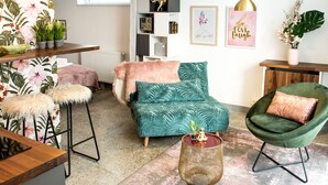 A modern living room with a teal sofa, a green armchair, and a wooden coffee table. There are potted plants, a radiator, and framed artwork on the walls. - Nikolai Homes (Vienna)