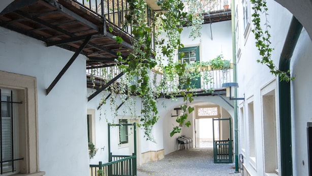 A cobblestone courtyard with a wooden staircase, white walls, and green railings. - Nikolai Homes (Vienna)