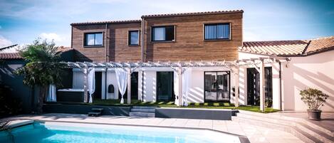 Una casa moderna de dos pisos con piscina, un patio cubierto y un césped bien cuidado.