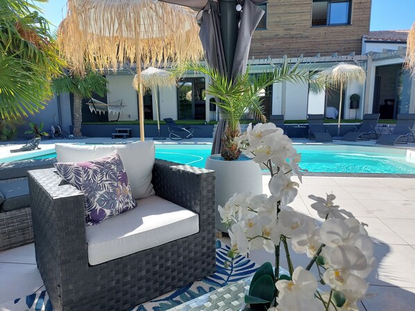 A poolside area with a wicker sofa, a thatched umbrella, and white orchids.
