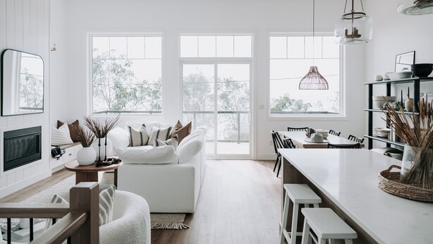 A modern kitchen with white cabinetry, a dining area with a white table and chairs, and large windows providing natural light.