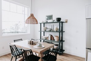 A modern kitchen with a wooden table, black chairs, a black metal shelving unit with dishes, and a hanging light fixture. - 180 degree lake view, luxury Port Stanley escape overlooking the beach! (Port Stanley)