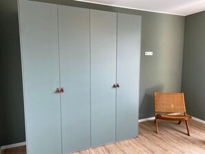 Una habitación con un armario amplio, una silla de mimbre y un enchufe de pared.
