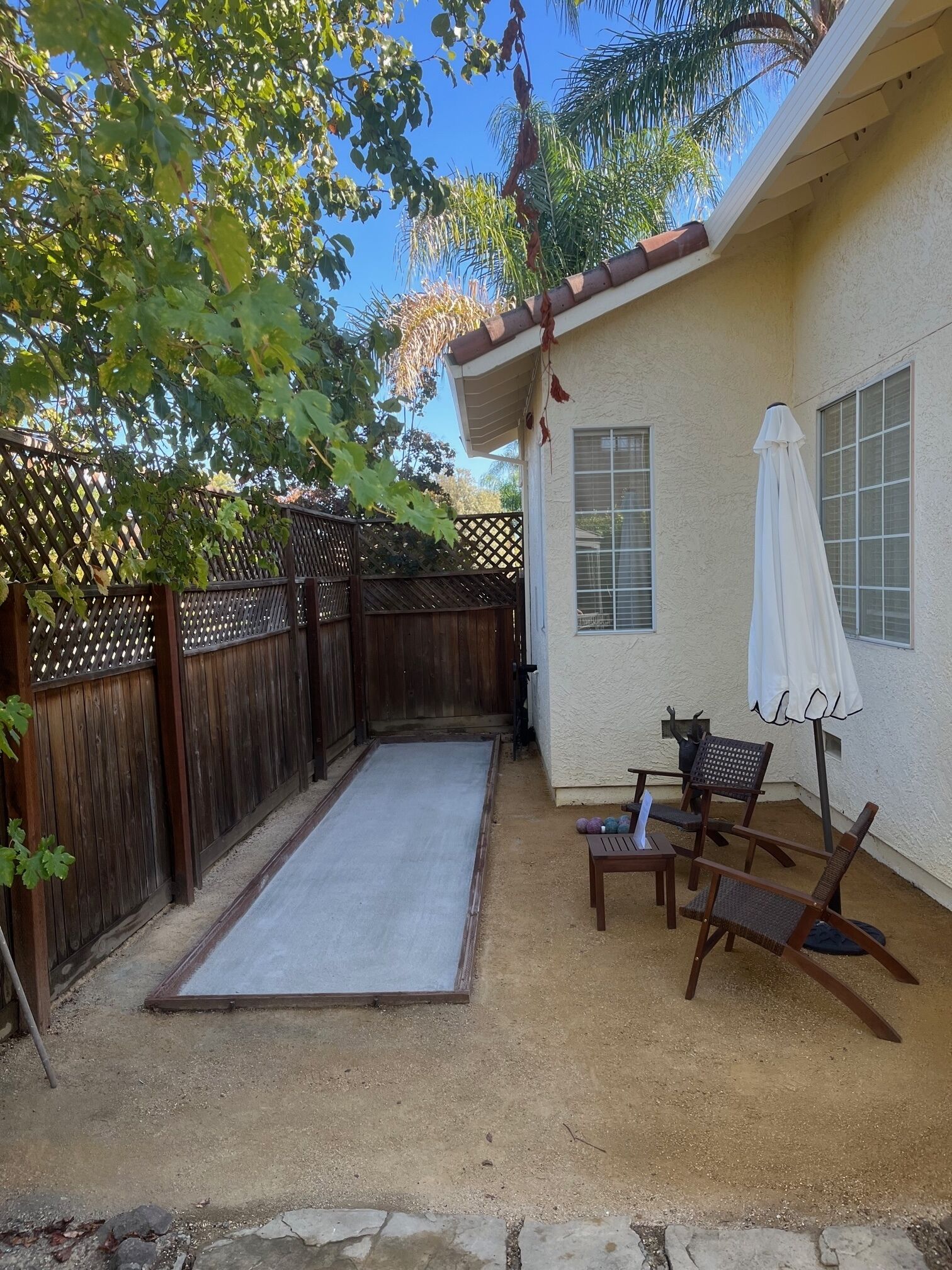 A backyard with a wooden fence, a patio with a table and chairs, and a white umbrella.