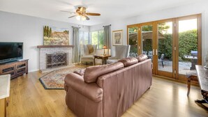 A spacious living room with a large leather sofa, a fireplace, a television, and a sliding glass door leading to an outdoor area. - Beautiful Home in Northwest Napa

 (Napa)