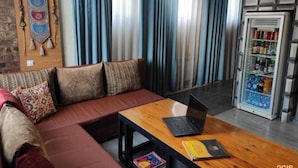 Ein modernes Wohnzimmer mit einer Couch, einem Couchtisch mit einem Laptop und einem Buch, einem Wandbehang und einem Kühlschrank mit Getränken.