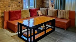Ein gemütliches Wohnzimmer mit einem Holztisch, einem orangefarbenen Ledersofa und gemusterten Kissen.