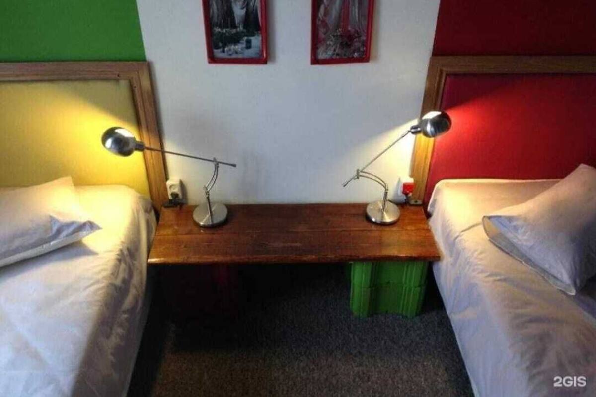 A room with two single beds, a wooden nightstand between them, two wall-mounted lamps, and two framed pictures on the wall.