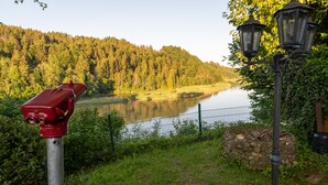 Un hidrante rojo, un muro de piedra y una valla metálica cerca de un lago con una colina boscosa al fondo.