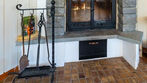 Una chimenea de piedra con una puerta negra, un estante encima y suelo de baldosas.