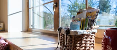 A room with large windows, a wicker basket with magazines, and a red mug on the windowsill.
