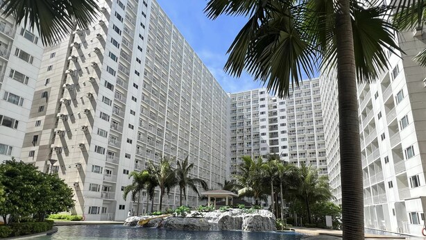 A modern high-rise building with a central pool, surrounded by palm trees and lounge chairs. - Shore One condotel at Mall of Asia, Pasay City Manila Philippines  (Pasay)