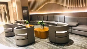 A modern lounge area with a curved sofa, round ottomans, and a wooden coffee table. - Shore One condotel at Mall of Asia, Pasay City Manila Philippines  (Pasay)