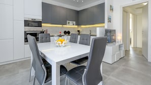 A modern kitchen with grey cabinets, a white dining table, and a bowl of fruit.