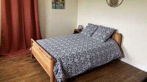Ett sovrum med en säng i trä, en röd gardin, en väggdekoration med fåglar, en rund väggdekoration och ett nattduksbord med en lampa.