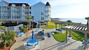 Un hotel frente a la playa con varios balcones, mobiliario exterior y zona de piscina.