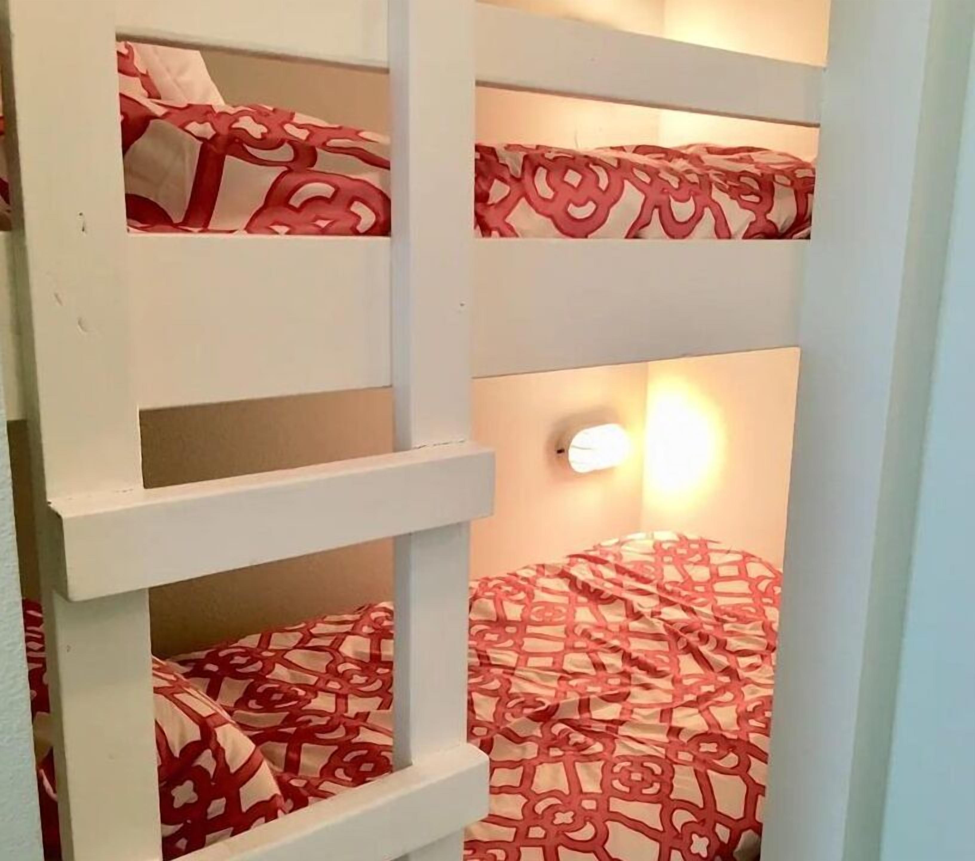 A bunk bed room with a patterned bedspread and a wall-mounted light fixture.