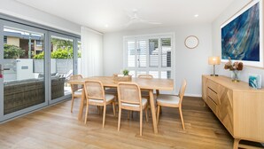 Een moderne eetruimte met een houten tafel en stoelen, een plafondventilator en een groot raam met jaloezieën.