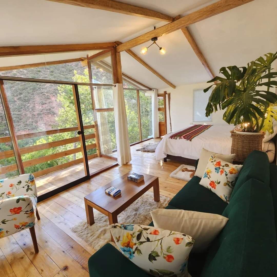 Una habitación amplia con una cama grande, un sofá verde, una mesa de centro de madera y un ventanal con vistas al exterior.