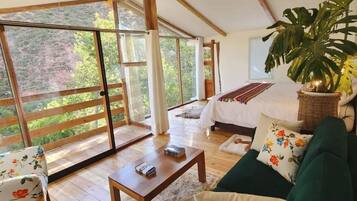 Una habitación amplia con una cama grande, un sofá verde, una mesa de centro de madera y un ventanal con vistas al exterior.