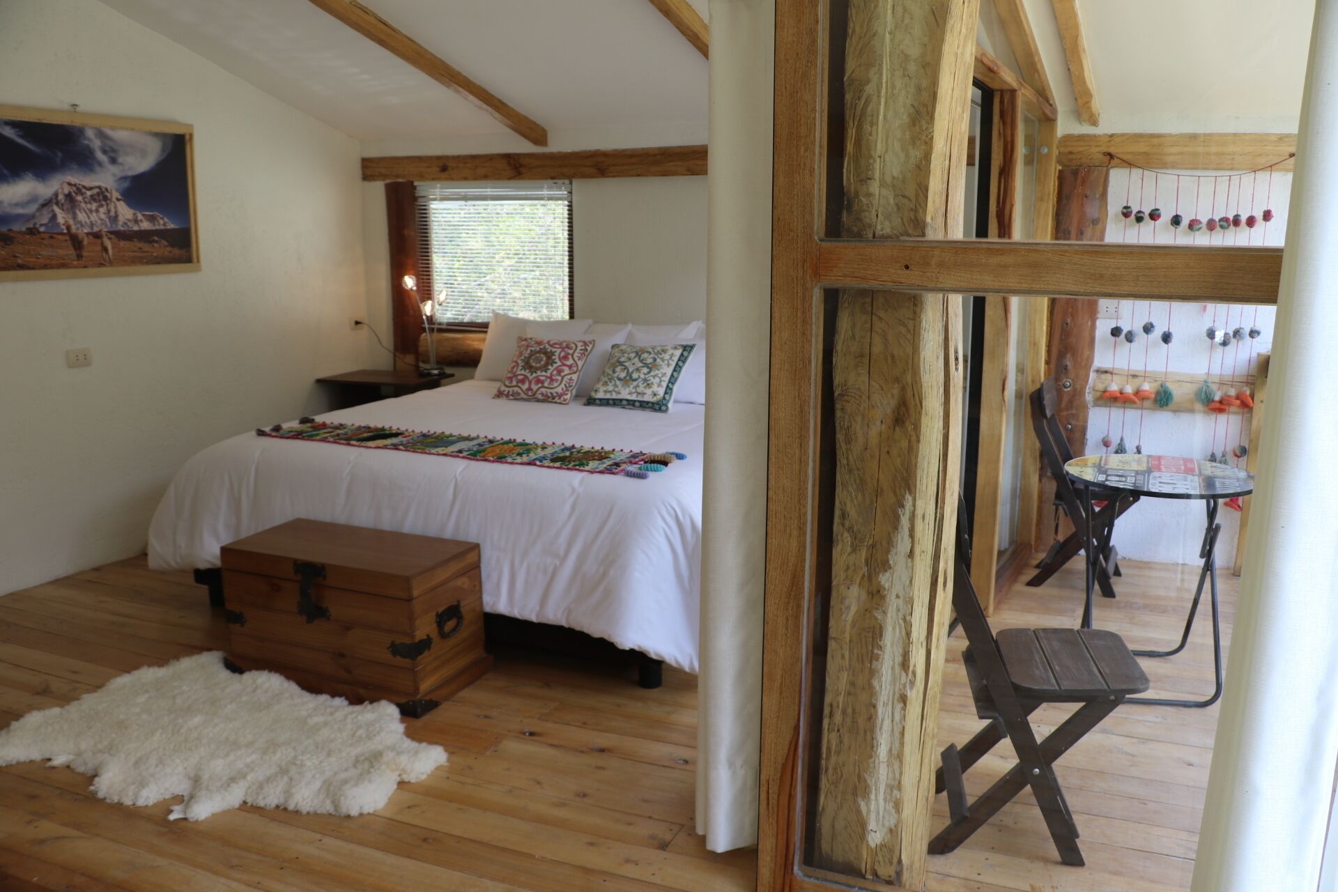 Una camera da letto con pavimento in legno, un letto con biancheria bianca, un baule di legno e una stuoia di pelliccia.