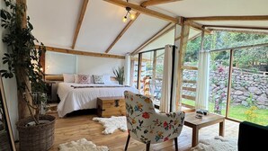 Amplia habitación tipo tienda con cama, silla, una mesita y vistas al jardín a través de amplios ventanales.