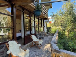 Eine Holzterrasse mit zwei weißen, flauschigen Stühlen, einer Steinmauer und einem hängenden Blumentopf.
