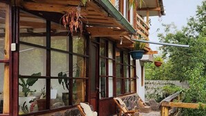 Una casa de madera con base de piedra, ventanas grandes y un porche cubierto con dos sillas de madera.