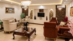 A living room with a chandelier, sofas, a TV, and decorative wall art. - Aziz Egypt Pyramids Hotel (Giza)