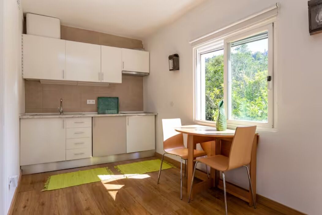 Una cucina compatta con mobili bianchi, un tappeto verde e una finestra vista verde.