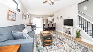 A modern living room with a grey sofa, a ceiling fan, a television, and a patterned rug. - Charming 3-bedroom, 2 bathroom house with outdoor space in Winona (Winona)
