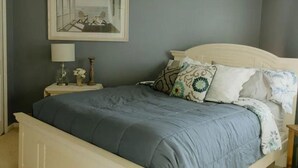 Een slaapkamer met een bed, een nachtkastje, een lamp en een ingelijst schilderij aan de muur.