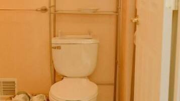 A small bathroom with a toilet, a metal shelf unit above the toilet, and a wicker basket on the floor.