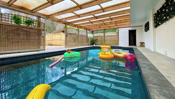 A swimming pool with a wooden ceiling and glass panels, surrounded by a wooden fence and plants. - 1 bedroom accommodation in Camerton, near Bath (Camerton, near Bath)