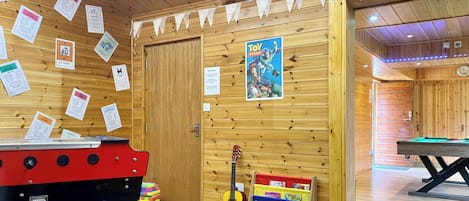 Una sala de madera con una mesa de billar, un dardo y una guitarra. Hay carteles en la pared y un póster de 'Toy Story'.