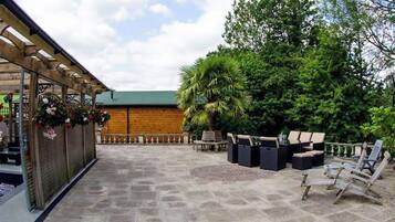 A patio area with stone flooring, outdoor seating, and a wooden pergola with hanging flowers.
