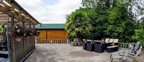 A patio area with stone flooring, outdoor seating, and a wooden pergola with hanging flowers.