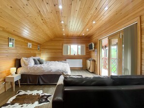 A wooden cabin bedroom with a bed, a sofa, a cowhide rug, a TV, and a window.