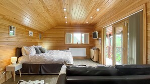 A wooden cabin bedroom with a bed, a sofa, a cowhide rug, a TV, and a window. - 1 bedroom accommodation in Camerton, near Bath (Camerton, near Bath)