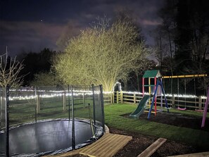A playground with a trampoline, slide, and swing set at night.