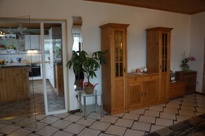 A spacious living area with a wooden cabinet, a glass table with a potted plant, and a kitchen in the background. - Gemütliche Erdgeschosswohnung mit Terrasse in Ortsrandlage in Waibstadt (Waibstadt)