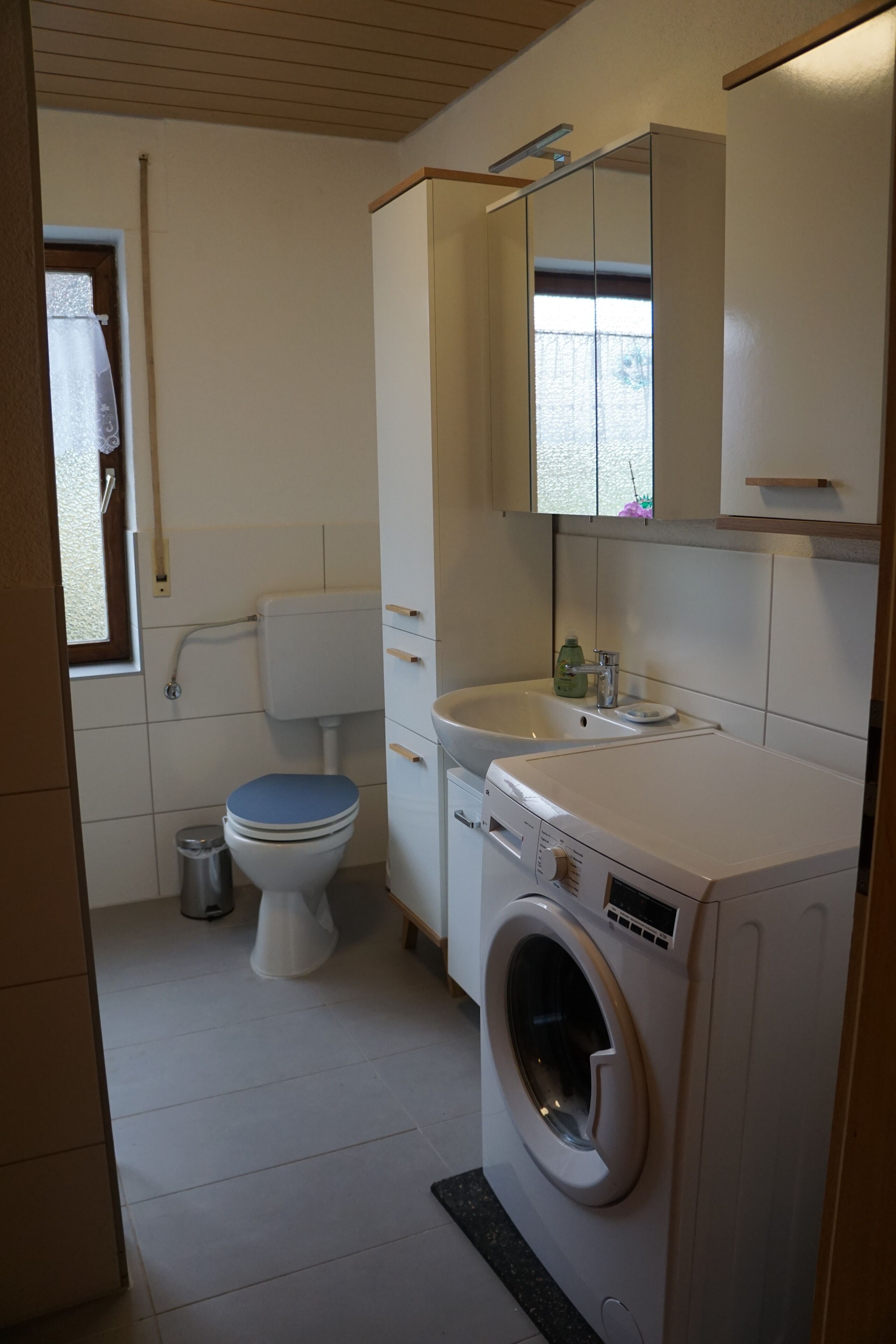 A compact bathroom with a toilet, sink, and washing machine.