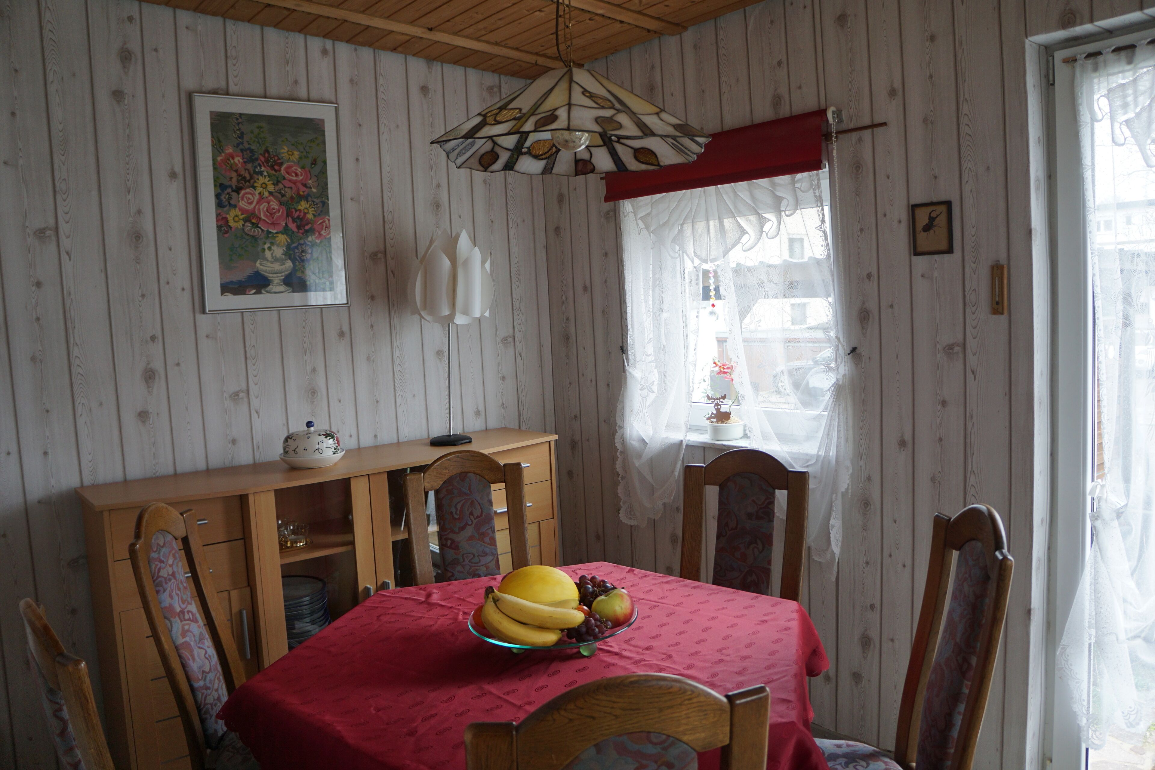 Zona de menjador amb taula de fusta, cadires, estovell vermell i un plat de fruita.