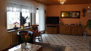 A living room with a TV, wooden cabinets, a rocking chair, and a large window with curtains. - Gemütliche Erdgeschosswohnung mit Terrasse in Ortsrandlage in Waibstadt (Waibstadt)