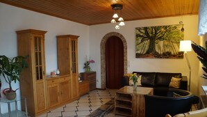 A living room with a wooden cabinet, a black leather sofa, a coffee table, and a painting of a tree. - Gemütliche Erdgeschosswohnung mit Terrasse in Ortsrandlage in Waibstadt (Waibstadt)