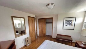 Un dormitorio con cama, armario de madera, un banco, un cuadro enmarcado y un espejo.